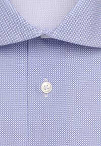 Chemise bleu clair avec un petit motif circulaire bleu foncé, bouton blanc fixé sous un col pointu.