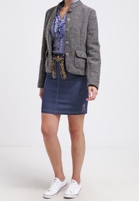 Giacca in misto lana grigia con bottoni, camicia a quadri blu, gonna di jeans con cuciture decorative e sneakers bianche.