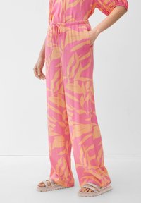 Roze en gele, gebloemde, wijduitlopende broeken met een elastische tailleband en zijzakken. Gecombineerd met lichtgekleurde, sandalen met bandjes.