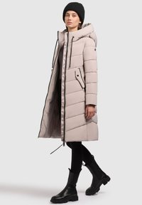 Gai bežs pūka mētis ar kapuci, ar rāvējslēdzēju priekšā, ar diognālu šuvju un sānu kabatām. Uzvilkts ar melniem legingiem un potītes zābakiem.