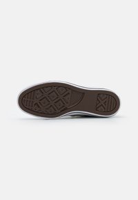 Brown rubber outsole with diamond traction pattern, white sidewalls, and textured accents, designed for grip and durability.