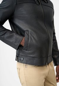 Black leather jacket with a textured surface, zip closure, and side pockets. Features a straight cut and subtle stitching details.
