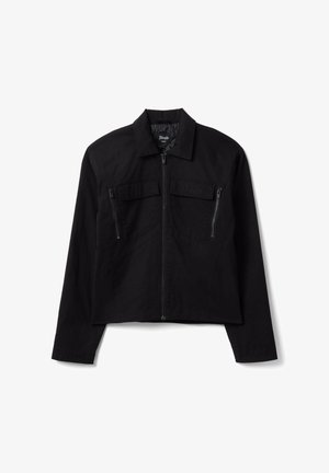 Chaqueta negra con cremallera y cuello, dos bolsillos en el pecho con cremalleras y solapas, y mangas largas, exhibida sobre fondo blanco.