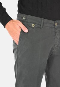 Pantaloni in cotone grigi con una superficie liscia, dotati di due tasche frontali, vita con bottone e dettagli di cucitura discreti.
