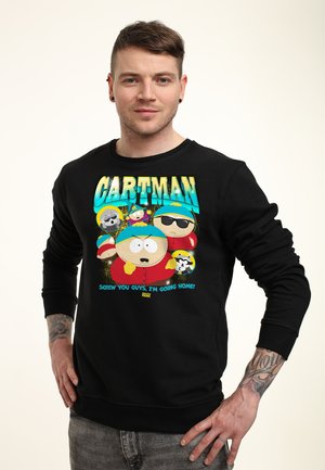 Młody mężczyzna z kolczykami i tatuażami noszący czarną bluzę z animowaną postacią Cartmana i napisem „Screw you guys, I'm going home!”