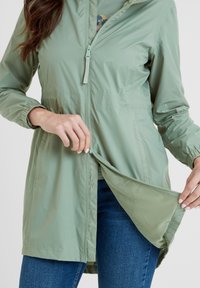 Light green, zip-front jacket with long sleeves and mesh lining. Features elastic cuffs and a straight cut. Material is smooth and lightweight.