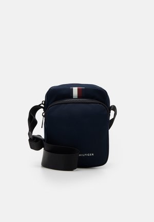 Marineblå crossbody-taske lavet af nylon med lynlås, justerbar rem og et rødt, hvidt og blåt stribet accent.