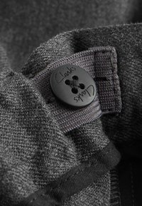 Grauer Stoff mit einer schwarzen Knopfleiste, auf der "Clarks" eingraviert ist. Der Knopf hat vier Löcher und befestigt ein Kleidungsdetail.