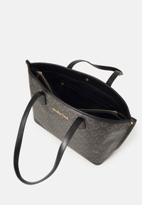 Saco tote preto com exterior texturizado apresentando um padrão de logótipos subtil, ferragens douradas e alças de couro. Parte superior aberta com bolsos interiores.