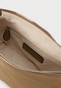 Hnedé puzdro na zips vyrobené z hladkého materiálu, s béžovým interiérom, vnútornou kapsou s hnedým akcentom a značkovou etiketou.