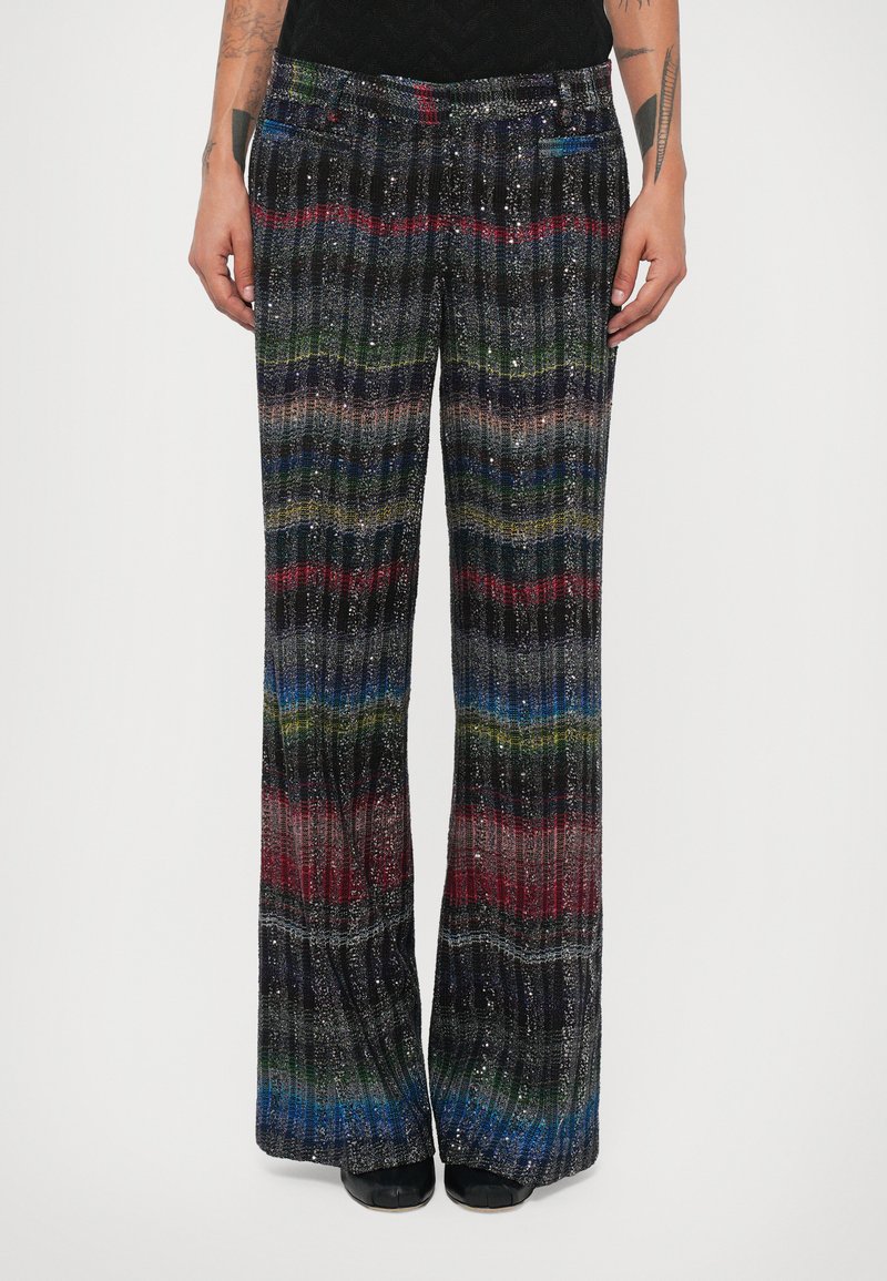 Pantalons larges noirs et multicolores avec une texture côtelée, ornés de rayures horizontales en rouge, bleu, vert et paillettes argentées.