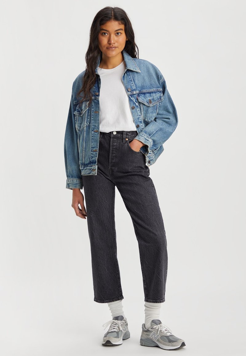 Veste en denim, bleu clair ; T-shirt blanc ; jeans noirs taille haute ; baskets grises ; chaussettes neutres. Comprend une fermeture à boutons sur le devant et des poches latérales.