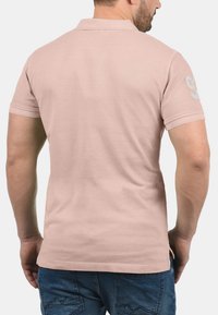 Polo shirt met korte mouwen in lichtroze stof, met een subtiele textuur en het nummer 93 gedrukt in een zachte blauwtint op de linker mouw.