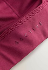 Tessuto atletico bordeaux con una texture liscia presenta cuciture impunturate e un logo in rilievo che scrive "ACTIVE" lungo il bordo.