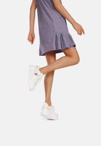 Sneaker platform bianchi con borchie decorative argentate, abbinati a un abito lavanda fino al ginocchio con orlo svasato.