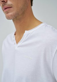 Weißes Baumwoll-T-Shirt mit Henley-Ausschnitt, ausgestattet mit drei Knöpfen und dezentem "SALSA JEANS" Stickerei auf der linken Vorderseite.
