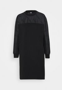 Schwarzes Kleid mit langen Ärmeln, ausgestattet mit einem strukturierten oberen Abschnitt und einem weichen Baumwollkörper. Die Ärmel besitzen ein dezentes Logo-Muster.