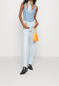 Denim korsett topp i ljusblått med framknäppning, parat med ljusblå raka jeans med sidoklyftor. Tillbehören inkluderar en liten orangeväska.