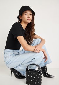 Černá krátká košile s krátkým rukávem, světle modré džíny s širokými nohavicemi, černé vysoké boty na podpatku a malá černá kabelka se stříbrnými cvočky.