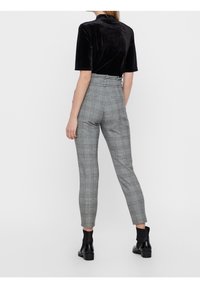 Pantalon taille haute à carreaux gris avec une coupe ajustée, jambes fuselées, et une légère brillance. Associé à des bottines noires. Texture lisse.