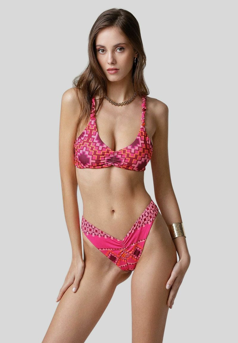 Bikini rosa a fantasia con design geometrico; il top ha spalline arricciate, mentre il fondo presenta una forma a V con decorazioni.