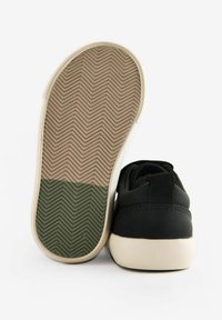 Zwarte sneaker met een glad bovenwerk en een twee-gekleurde rubberen zool met een visgraatpatroon; achterste lus voor gemakkelijke aan- en uittrekken.
