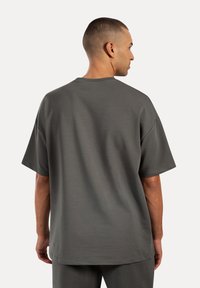 Grå oversized T-shirt lavet af glat stof, med korte ærmer, rund halsudskæring og en afslappet pasform, set bagfra.