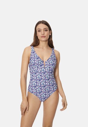 Mujer con un bañador de una pieza azul con estampado floral, escote en V profundo y una pequeña muesca frontal, posando frente a un fondo liso.