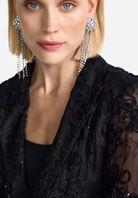 Mustad must õhuke jakk roosade aplikaatide ja sädelevate detailidega. Mudel kannab suuri sädelevaid ripatsitega kõrvarõngaid. Suletud fookus detailidele.