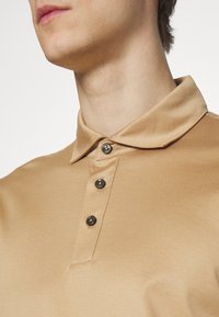 Ljus polo-skjorta i mjukt tyg, med en klassisk krage, tre mörka knappar och diskreta sömnadsdetaljer.