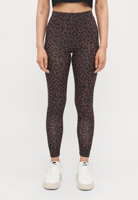 Legging sa uzorkom leopard u smeškoj i crnoj boji, napravljeni od rastezljivog materijala, upareni sa belim patikama. Imaju visok struk i prianjajući dizajn.