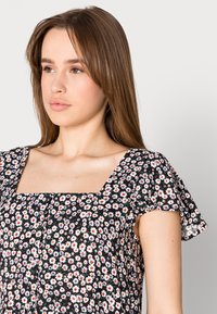 Vestido floral com mangas curtas e esvoaçantes, decote quadrado e base preta com margaridas brancas e vermelhas, feito de tecido leve.