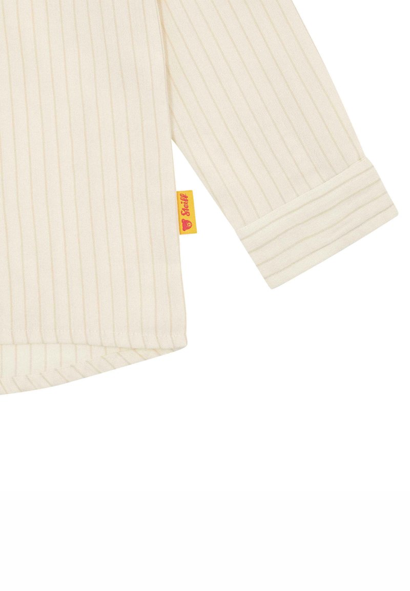 Cremfarbige Hemd mit feinen vertikalen Streifen, langen Ärmeln und aufgerolltem Bund. Verfügt über ein kleines, gelbes und rotes, angenähtes Etikett.