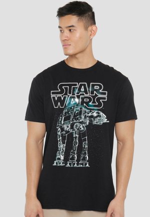 Man wearing black Star Wars t-shirt with AT-AT walker graphic looking to the side against a neutral background.