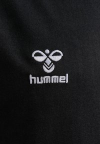 Tessuto nero con texture liscia, caratterizzato da un logo ricamato bianco che mostra un design stilizzato di un'ape e il nome del marchio "hummel" sottostante.