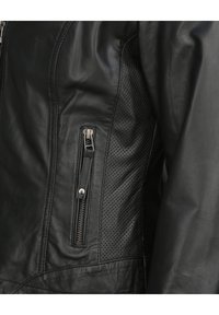 Närbild av en svart läderjacka som visar en vertikal dragkedjeficka och detaljer med perforerat läder.