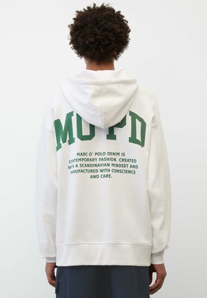 Sudadera blanca con gran texto en bloque verde en la parte de atrás, con texto impreso adicional que detalla la filosofía de la marca. Material de algodón, corte relajado.