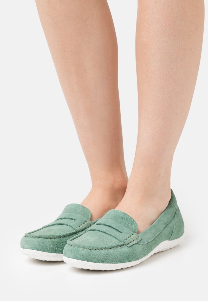 Mocassins en daim vert à profil bas avec une semelle en caoutchouc blanche, présentant une couture horizontale et un design classique sans lacets.