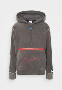 Felpa grigia realizzata in tessuto morbido, con una tasca con zip rossa, logo Nike rosso e cordino blu. Include patch NBA sulle maniche.