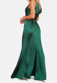Lång grön satin-klänning med kappa bak och slits på sidan. Mjuk textur och figurnära silhuett. Har en slank design och minimal metallaccessoarer.