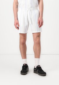 Hvide stribede shorts med snor i taljen, lavet af et struktureret stof, båret med sorte sneakers og hvide sokker.