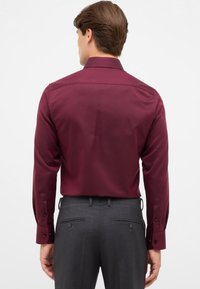 Bordeaux langemouwen overhemd met een soepele textuur en knoopmanchetten, gecombineerd met grijze broek met achterzakken en riemlussen.