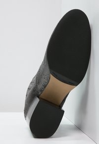 Schwarzer, strukturiertes Schuh mit niedrigem Absatz, der ein glattes Lederinterieur und eine Gummisohle mit einem gemusterten Grip zeigt.
