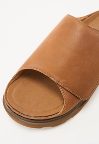 Sandalo a scivolo in pelle marrone con una larga fascia, una soletta morbida e testurizzata, suola curvata e cuciture a contrasto lungo il bordo.
