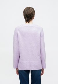 Prevelik jopič vijolične barve z teksturirano površino, rebrastim spodnjim robom in dolgimi rokavi; ima okrogel izrez in spuščena ramena.