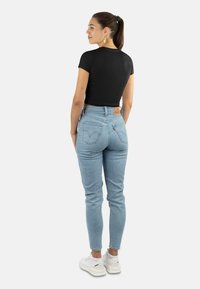Schwarzes kurzärmeliges Cropped-T-Shirt, kombiniert mit hellblauen hochgeschnittenen Jeans. Weiße Sneakers runden das Outfit ab. Rückansicht gezeigt.