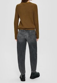 Maglione a coste marrone abbinato a jeans neri sbiaditi a vita alta. Scarpe con plateau nere completano l'outfit.