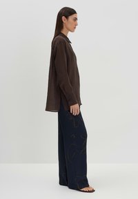 Brown, long-sleeve shirt with a collar, paired with wide-leg navy pants featuring a light brown abstract pattern, smooth texture, and relaxed fit.
