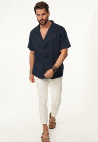 Marineblaues kurzärmeliges Button-down-Hemd mit strukturiertem Muster, kombiniert mit weißen strukturierten Hosen und hellbraunen Sandalenschuhen.