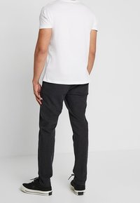 Biała koszulka z krótkim rękawem, szare spodnie i czarne trampki. Koszulka ma okrągły dekolt, a spodnie są dopasowane z bocznymi kieszeniami.